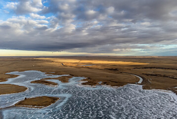 Aerial view of large cracks across Crawling Valley Reservoir and frozen tundra during winter in Alberta Canada.