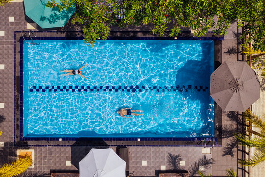 Swimmers man and woman couple diving and swimming in the luxury villa swimming pool. Aerial top shot. Careless summer vacation concept image.
