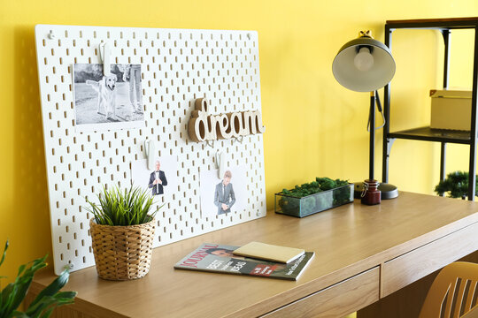 Stylish workplace with peg board on yellow wall background