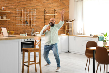 Funny bald man drinking beer and singing in kitchen
