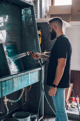 Male worker cleaning screen frame with water in a printing workshop