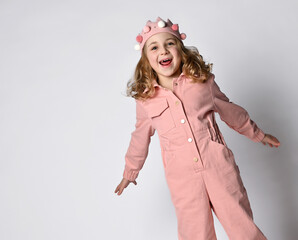 cute excited screaming girl with a plush crown, in a dusty pink cotton summer jumpsuit spread her hands in happiness.