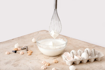 Whisk with meringue and chicken eggs on table