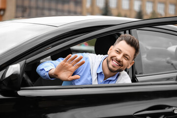 Handsome businessman waving hand in modern car