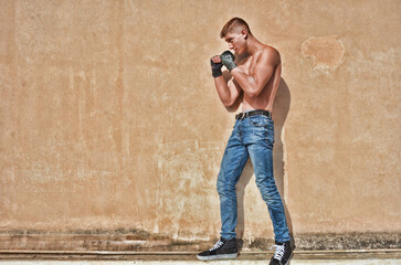 Fitness Model Fighter in Jeans doing Muay Thai Kickboxing Guard Stance against an old wall