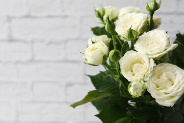 Bouquet of beautiful fresh roses near white brick wall, closeup
