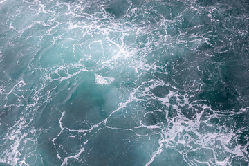Fototapeta na wymiar Water surface abstract background. White waves and foam on the blue sea water. Wake behind ship