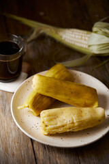 Humitas are savory steamed fresh corn cakes, a traditional Ecuadorian appetizer. It’s accompanied by coffee, on a wooden background. 
