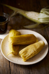 Humitas are savory steamed fresh corn cakes, a traditional Ecuadorian appetizer. It’s accompanied by coffee, on a wooden background. 