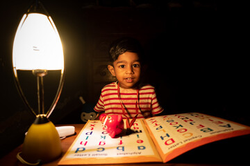 A boy learning the English alphabet using a charger lamp In the evening at home. Asian boy studying...