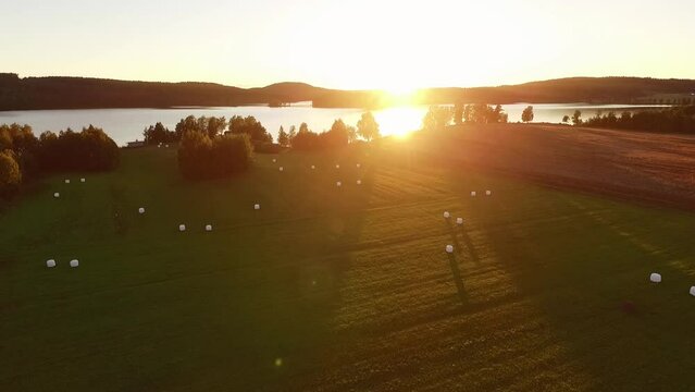 Beautiful sunset over lake and field with feed bales.