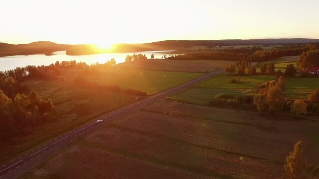 Aerial with beautiful sunset, lake and silver car driving on road.