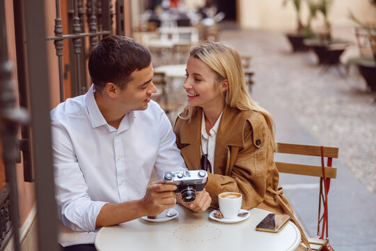 Smiling woman sitting at table of street cafe with handsome man and reviewing photos