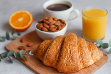 Croissant with orange juice, orange fruit, coffee and almond nuts on the table. Delicious french or continental breakfast. Selective focus, close-up
