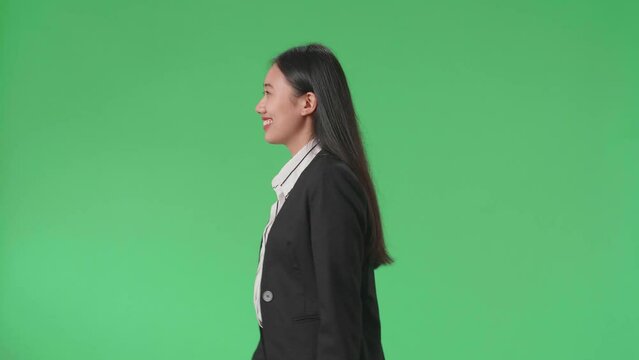 Side View Of A Smiling Asian Business Woman Walking Through Green Screen In The Studio
