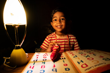 A boy learning the English alphabet using a charger lamp In the evening at home. Asian boy studying...