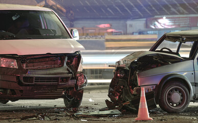 Damaged in heavy car accident vehicles after collision on city street crash site at night. Road...