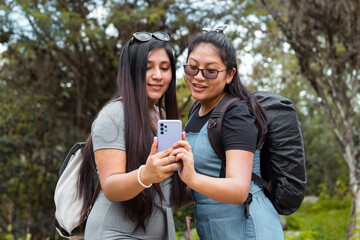 Mujeres jóvenes con cabello largo sorprendidas por algo en el móvil abrazándose en una parque,espacio libre,