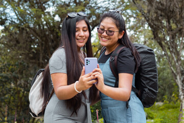 Retrato de dos hermosas chicas tomándose fotos en un parque,
Amigas felices revisando teléfono...