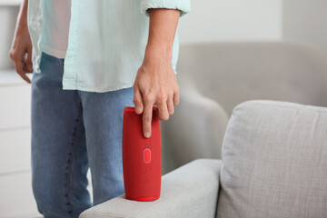 Man turning on wireless portable speaker on sofa, closeup