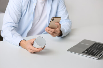 Man connecting mobile phone to wireless portable speaker on table, closeup