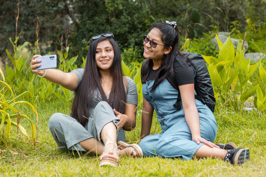 Retrato de dos hermosas chicas tomándose fotos en un parque,
Amigas felices revisando teléfono inteligente en aire libre,