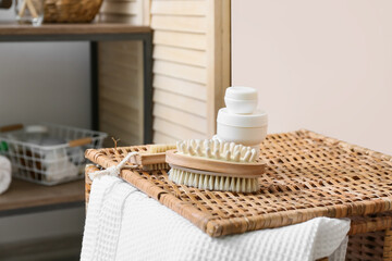 Fototapeta na wymiar Body brushes and jars with cosmetic products on wicker laundry basket near light wall