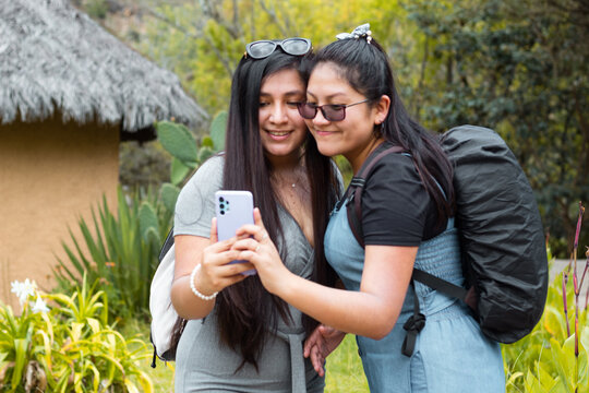 Retrato de dos hermosas chicas tomándose fotos en aire libre,
Amigas felices revisando teléfono inteligente en aire libre,Dos chicas usando el móvil en medio de un camino rodeado de montañas