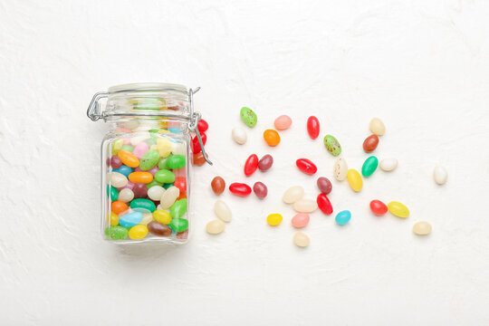 Glass jar with different jelly beans on light background