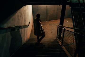 Man descending metal emergency stairs in the shadows of the night. Mystery and danger.