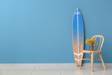 Vase with mimosa flowers on chair and surfboard near color wall in room