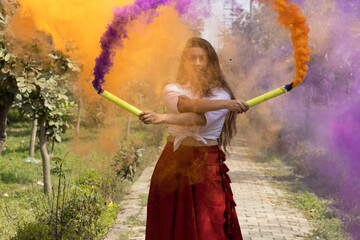 Beautiful young girl woman celebrate holi with colored multicolored smoke bombs of dry color Holi...