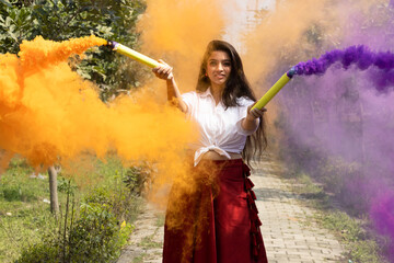 Holi festival - Beautiful young girl woman celebrate holi with colored multicolored smoke bombs of dry color Holi powder colour gulal abeer in the park in spring break