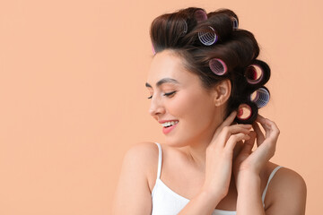 Fototapeta premium Beautiful young woman in hair rollers on color background
