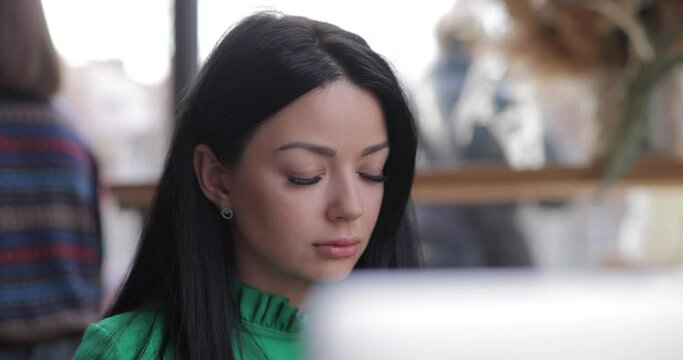 Freelancer woman works by laptop PC typing text sitting at the table in cafe wearing headphones