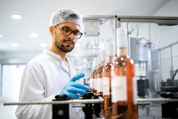 Technologist in white clothing and hairnet controlling production of beverage in wine bottling...