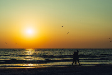 People walking along the beach in silhouette at sunset