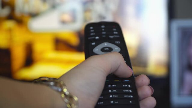 Pov woman hand holding TV remote control and changing chanels, increase volume, pov