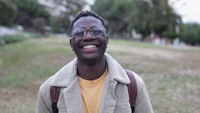 Smiling african young student man looking at camera outdoors - Cheerful 20s guy with backpack standing at university campus