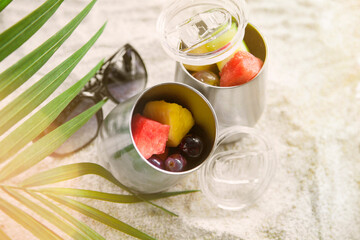 metal tumbler cups with tropical fruit sitting in sand on the beach