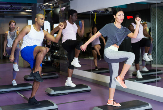 Multiethnic group of young adults training on step platforms in gym