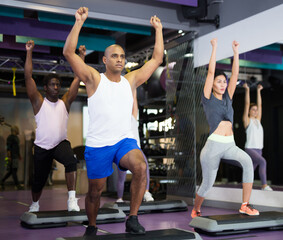 Portrait of young adult man training on step platform at group class in gym