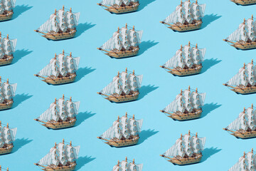 Small wooden home decoration pirate ship with white sails on a blue pastel ackground. Pattern....