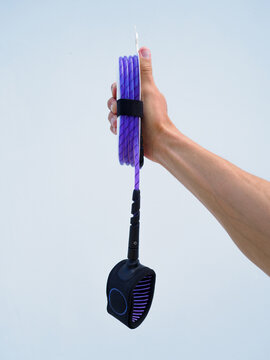 Hand holds new purple leash for surfing on white background.