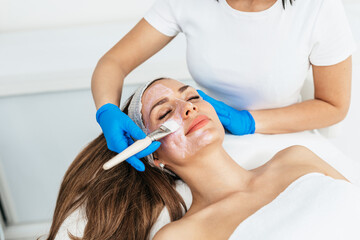 Beautiful woman receiving facial mask with rejuvenating effects in spa beauty salon