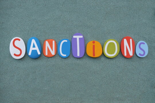 Sanctions, a threatened penalty for disobeying a law or rule, creative word composed with multi colored stone letters over green sand 