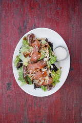 Caesar salad. Top view of fresh a Caesar salad with lettuce, parmesan cheese, bread croutons, smoked salmon, bacon and Caesar dressing, in a white dish on the restaurant table.
