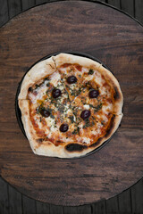 Traditional pizza. Top view of a mozzarella cheese pizza with tomato sauce, black olives and fresh oregano, on the wooden table.