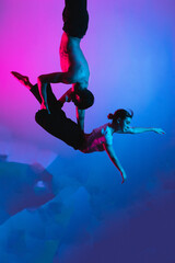 Fototapeta na wymiar Gymnastics support. A man with a girl perform an acrobatic exercise, neon light
