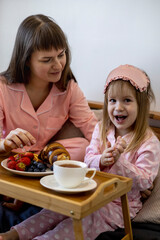 Beautiful young woman with a little cute girl spend time together at home, sitting on the bed.